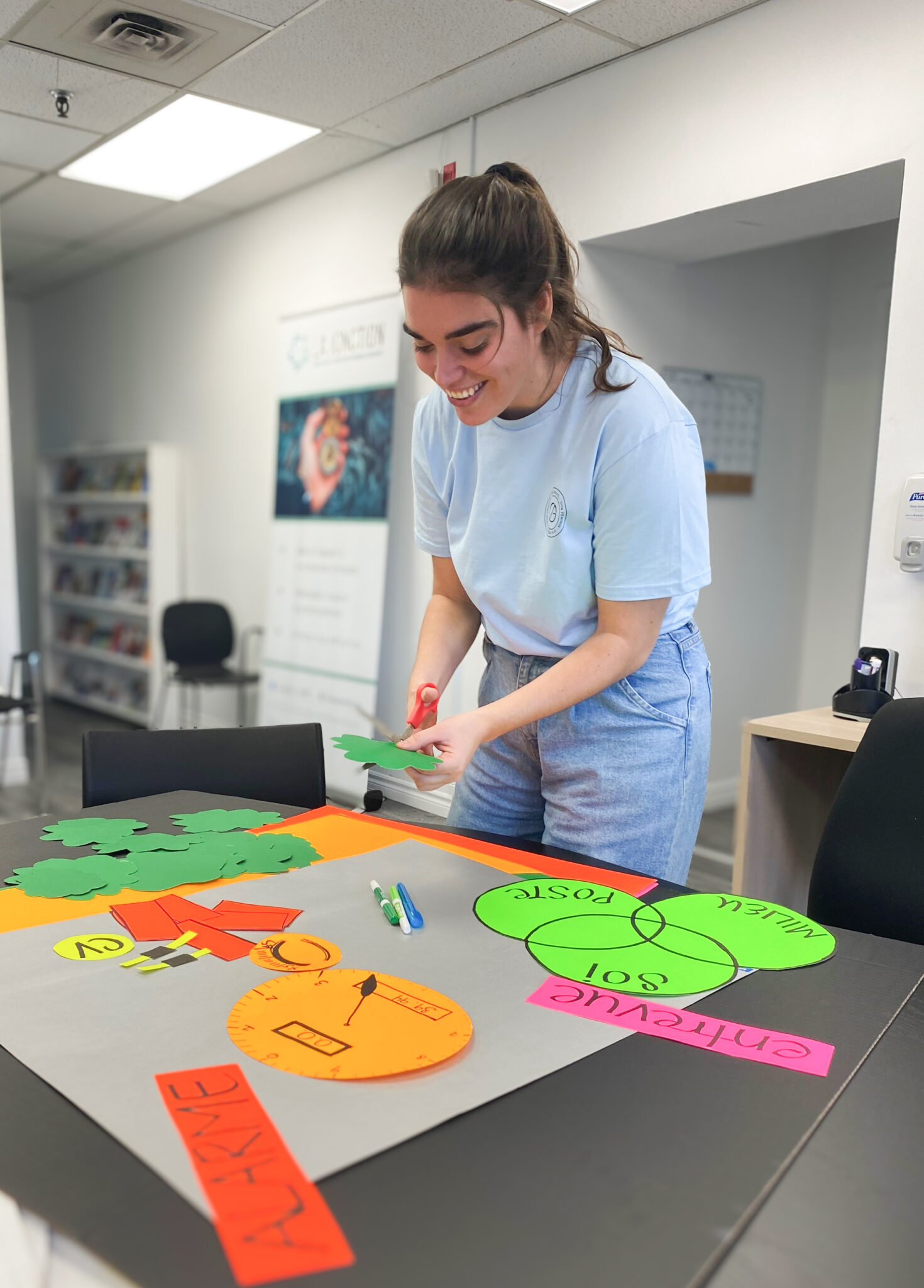 Une employée de la Jonction, lors d'un atelier, découpe des formes dans du carton coloré.